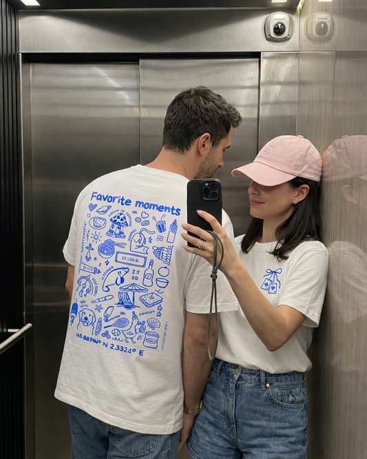 T shirts Koeur Indigo personnalisé portés par un couple dans un ascenseur qui font un selfie. Leurs t-shirts sont en communs avec leur souvenirs illustrés dessus.