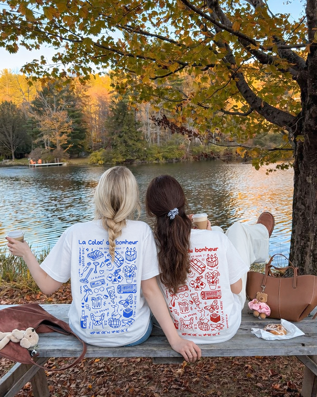 Deux meilleures amies qui portent des t shirts personnalisés Koeur Indigo en commun avec leurs souvenirs illustrés dessus. Elles sont devant un lac et font un picnic. 
