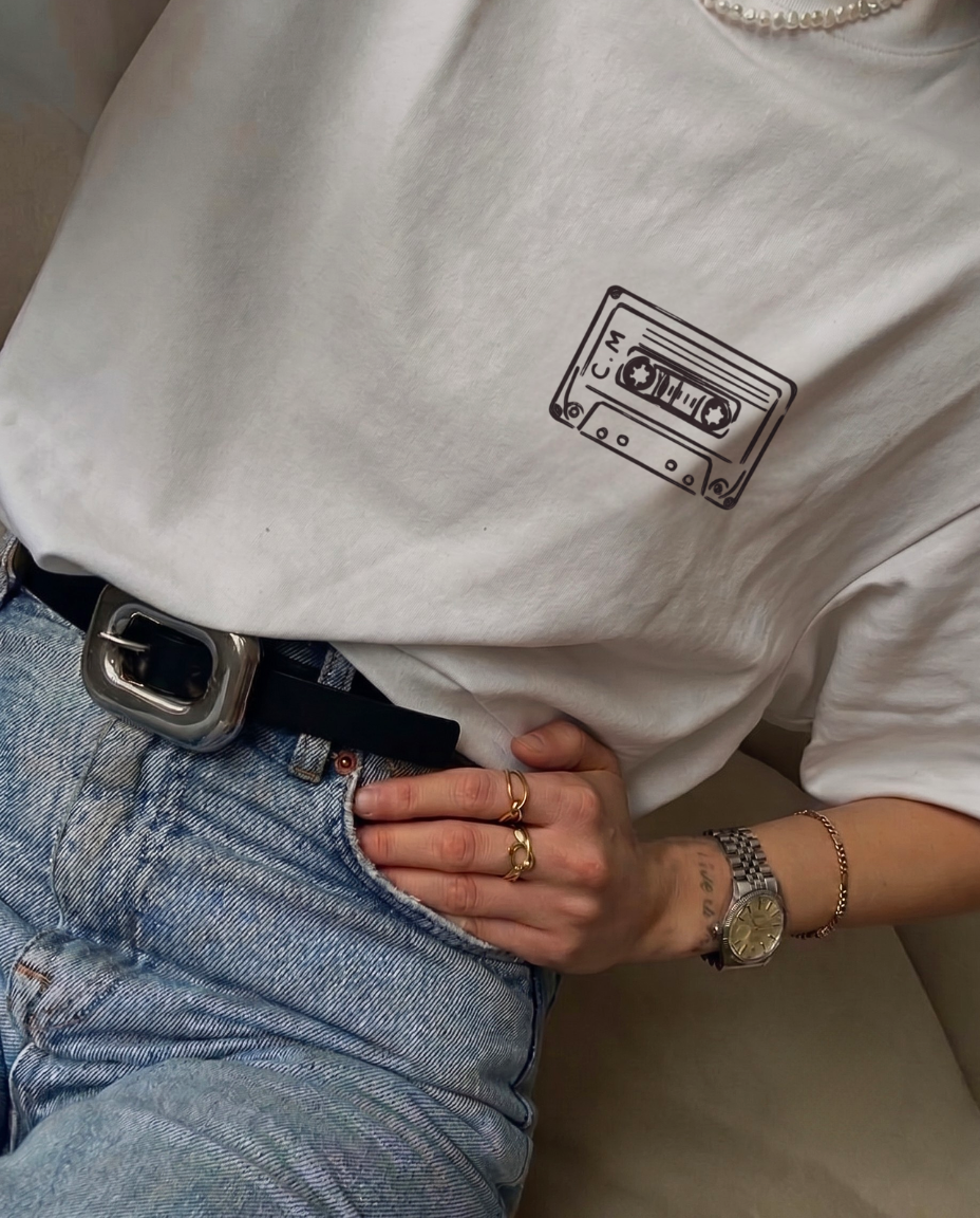 Photo portée du t-shirt Archives de la marque Koeur Indigo vu de devant avec le motif personnalisé d'une cassette audio vintage avec les initiales "C" et "M" dessinées sur la cassette.