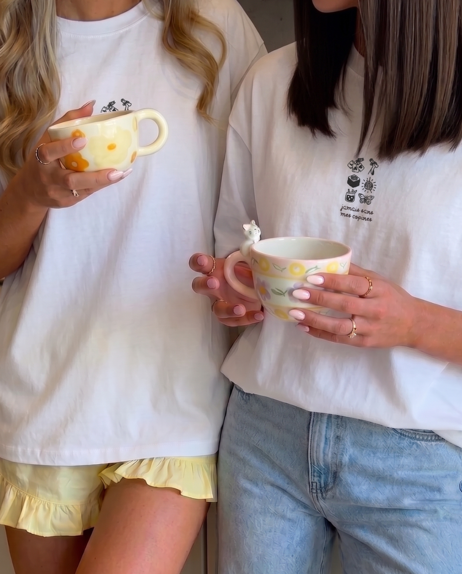 Deux meilleures amies portant des t-shirts personnalisés et assortis Koeur Indigo pour un look partagé en train de partager un moment complice en buvant un café. 